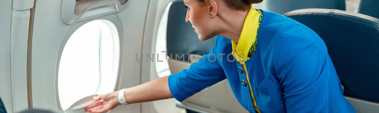 Female flight attendant opening window in airplane by Yaroslav_astakhov