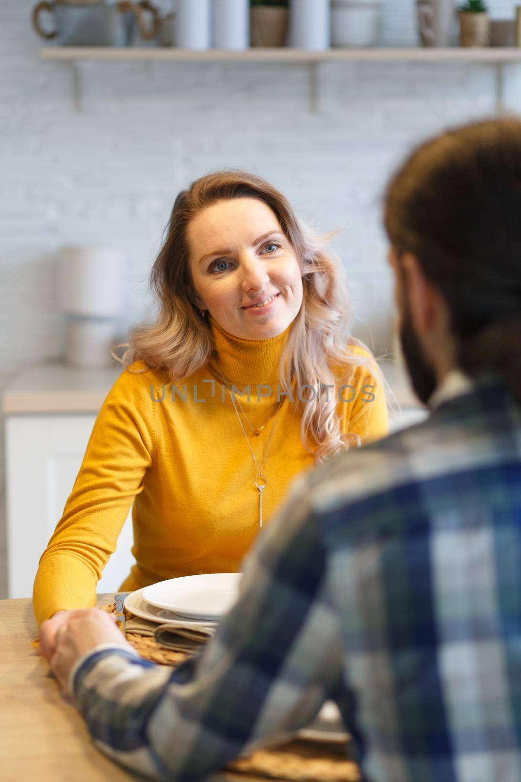 Beautiful couple having a conversation while looking at each other sitting at the table in a kitchen