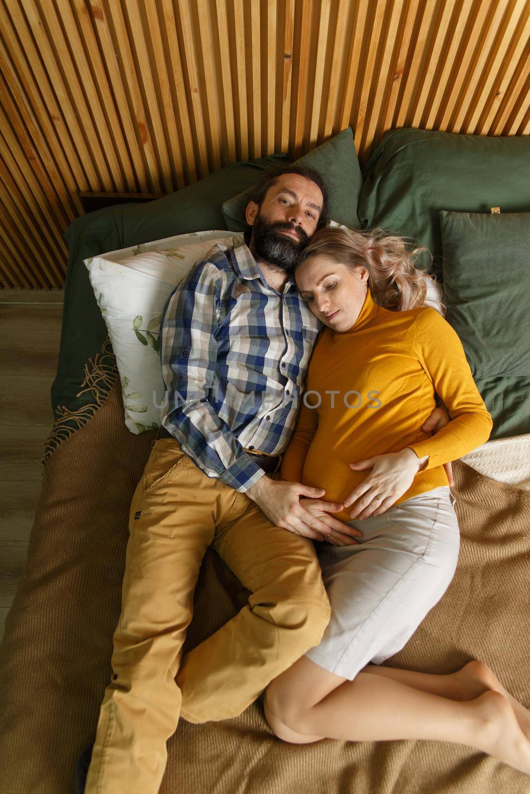 An adult couple in love waiting for a child. A man and his pregnant wife are basking in a bed in the bedroom