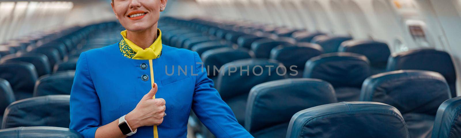 Smiling stewardess pointing at passenger seat in airplane cabin by Yaroslav_astakhov