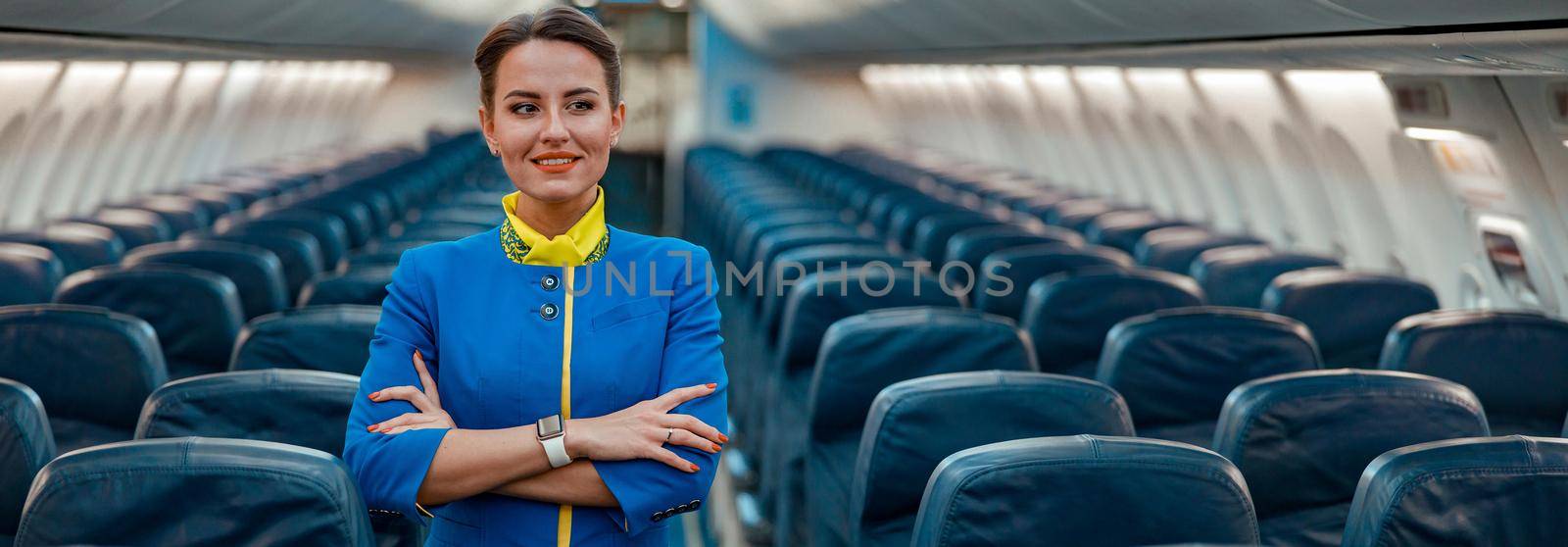 Joyful woman stewardess standing in aircraft passenger cabin by Yaroslav_astakhov