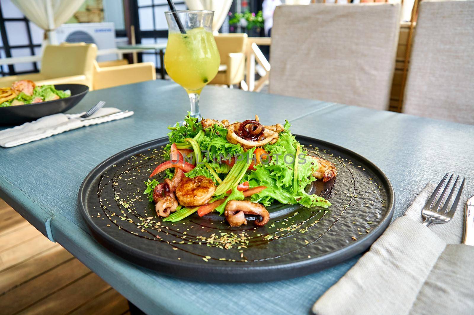 Fresh mediterranean salad with shrimps, octopus, and squid on a black plate on the veranda of the restaurant.