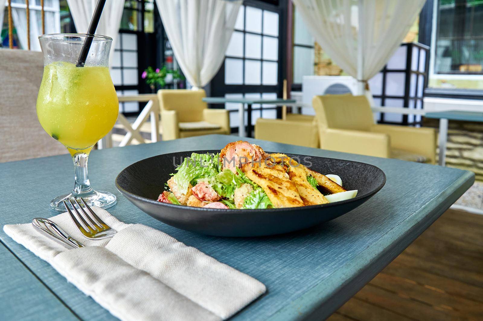 Fresh Caesar salad with chicken in a black bowl on the veranda of the restaurant.