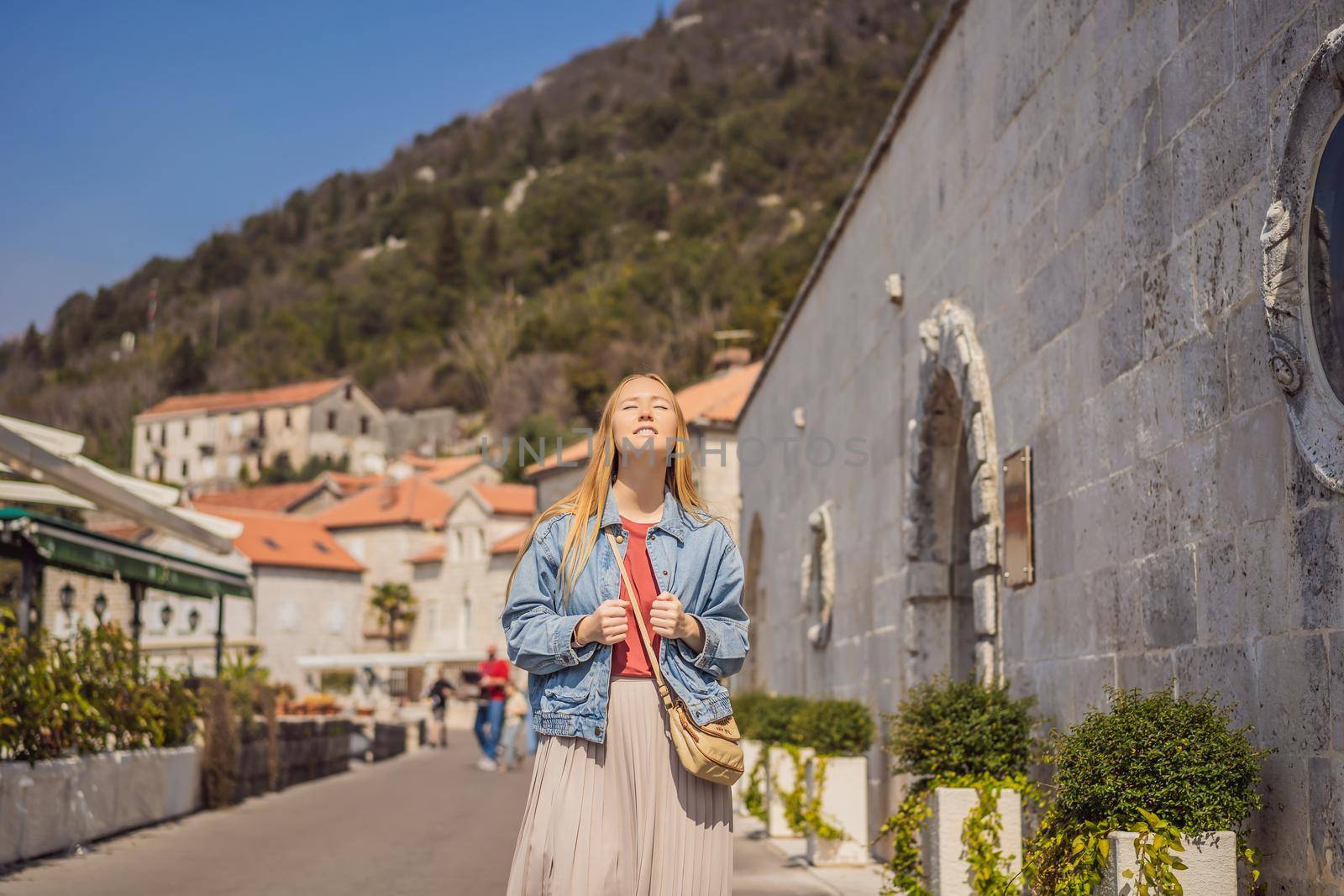 Woman tourist enjoying Colorful street in Old town of Perast on a sunny day, Montenegro. Travel to Montenegro concept. Scenic panorama view of the historic town of Perast at famous Bay of Kotor on a beautiful sunny day with blue sky and clouds in summer, Montenegro, southern Europe by galitskaya