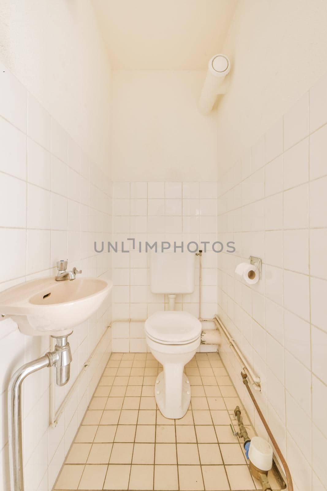 Modern flush toilet and ceramic sink installed on white tiled walls near mirror and towel in small restroom at home