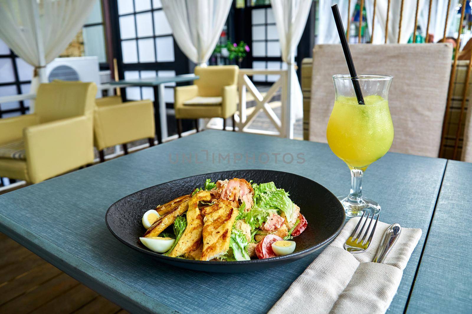 Fresh Caesar salad with chicken in a black bowl on the veranda of the restaurant.