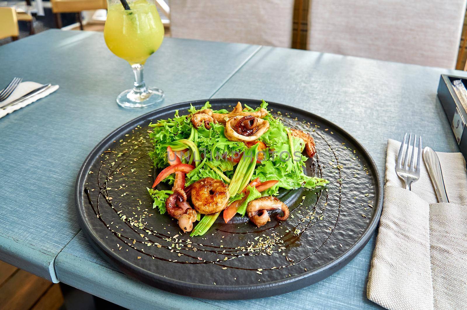 Fresh mediterranean salad with shrimps, octopus, and squid on a black plate on the veranda of the restaurant by Svetlana_Belozerova