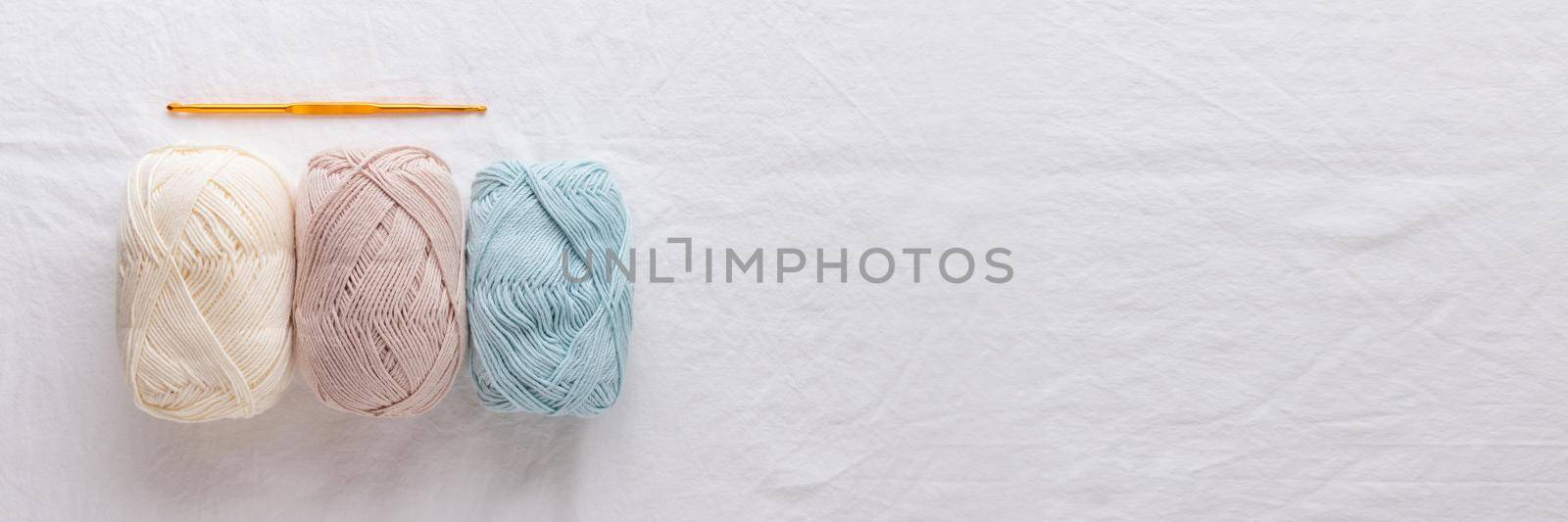 Needlework. Crochet hook and balls of cotton yarn pastel colors on a white table, copy space