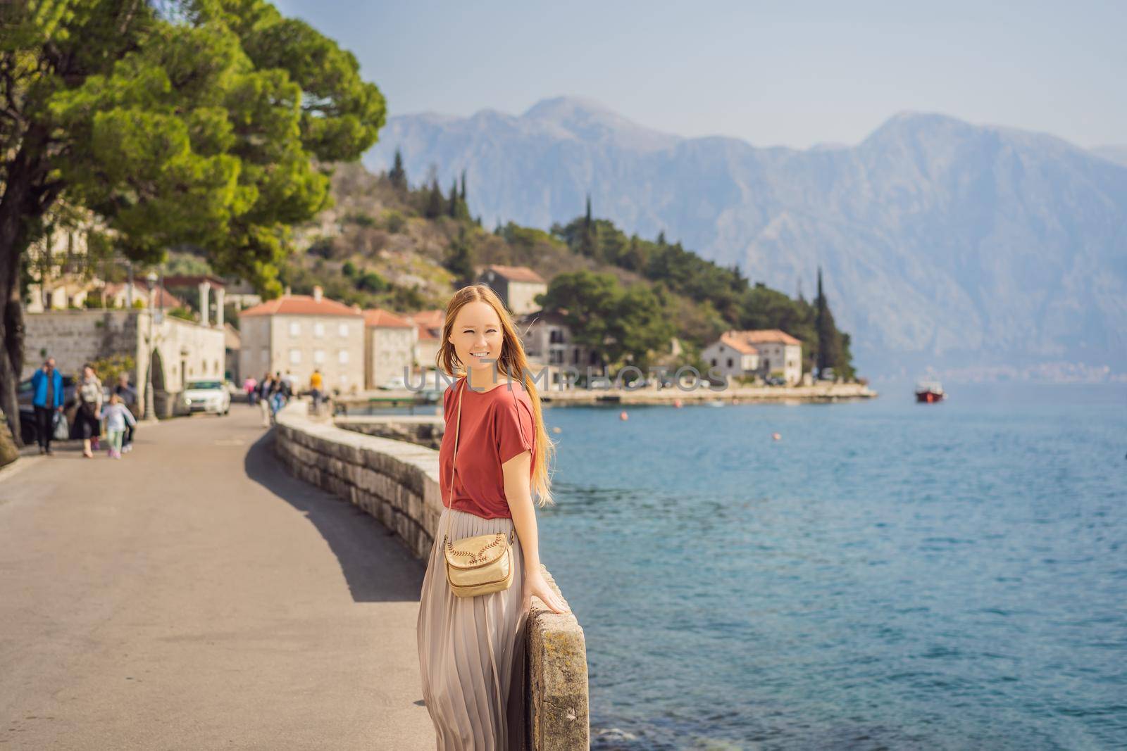 Woman tourist enjoying Colorful street in Old town of Perast on a sunny day, Montenegro. Travel to Montenegro concept. Scenic panorama view of the historic town of Perast at famous Bay of Kotor on a beautiful sunny day with blue sky and clouds in summer, Montenegro, southern Europe.