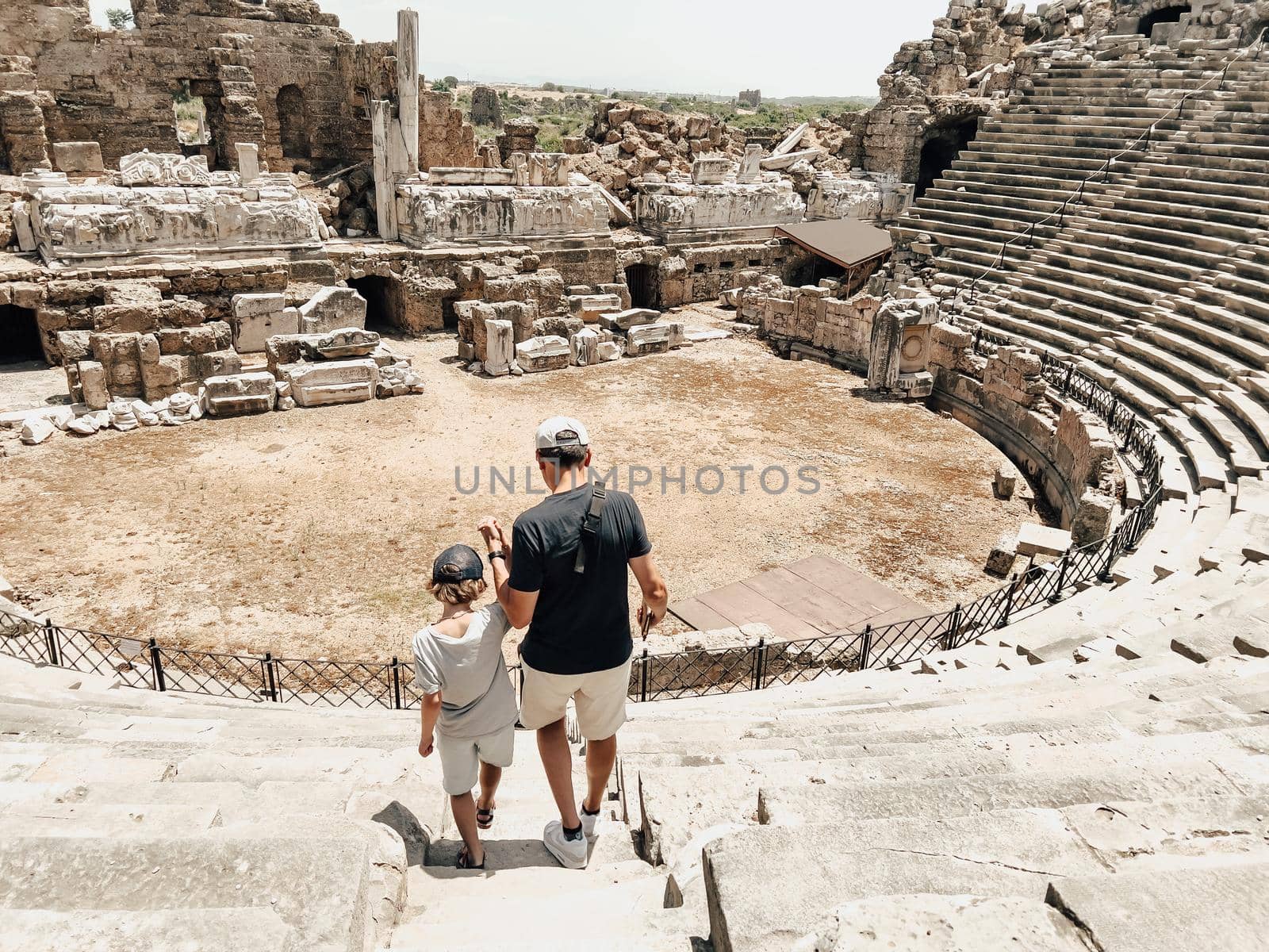 Young father dad and his school boy kid son tourists visiting ancient antique coliseum amphitheater ruins in hot summer day by Ostanina