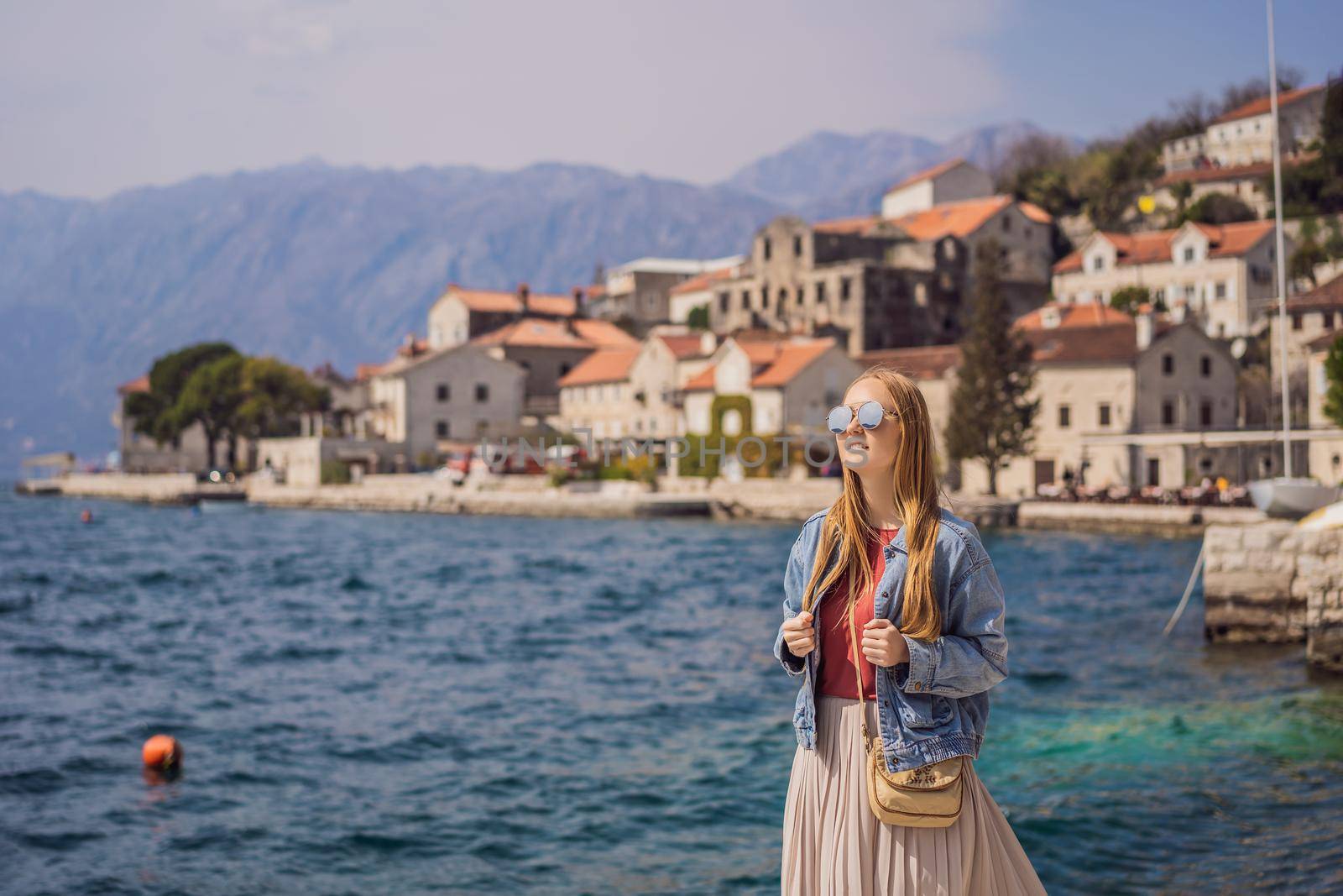 Woman tourist enjoying Colorful street in Old town of Perast on a sunny day, Montenegro. Travel to Montenegro concept. Scenic panorama view of the historic town of Perast at famous Bay of Kotor on a beautiful sunny day with blue sky and clouds in summer, Montenegro, southern Europe by galitskaya
