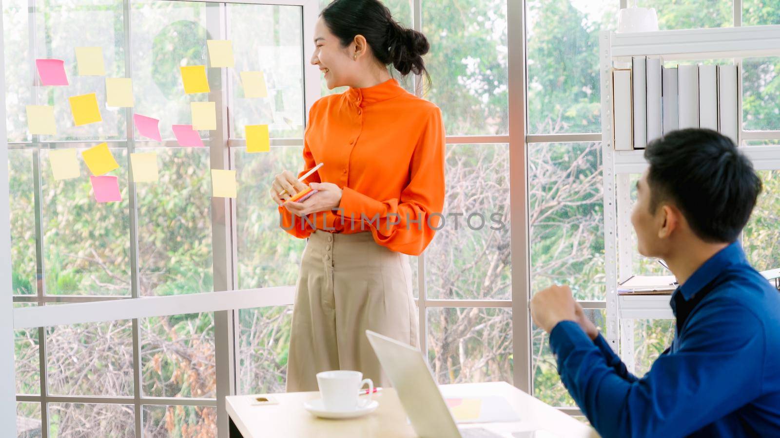 Business people work on project planning board in office and having conversation with coworker friend to analyze project development . They use sticky notes posted on glass wall to make it organized .