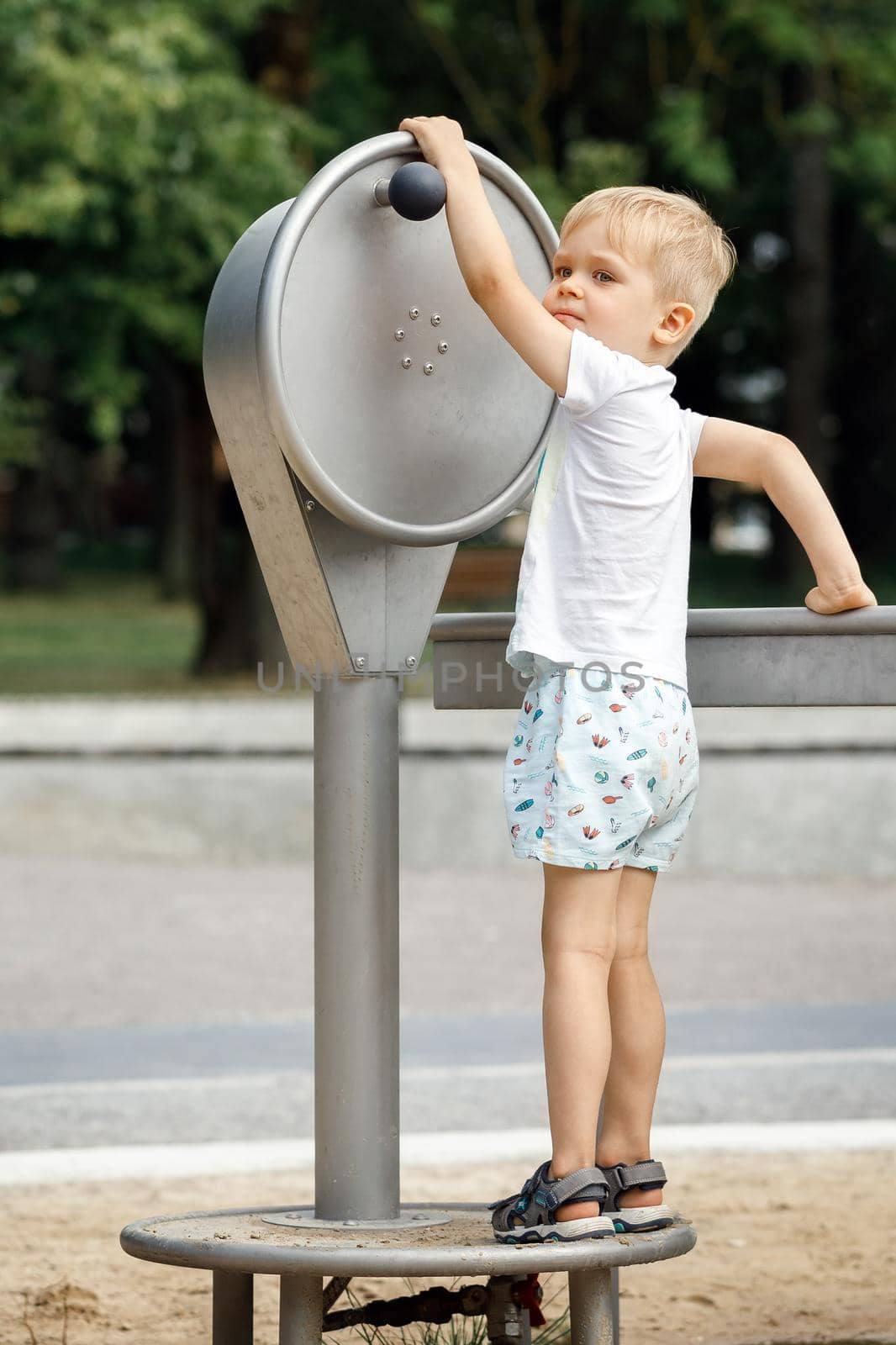 A little boy playing with a water pump in a city park.