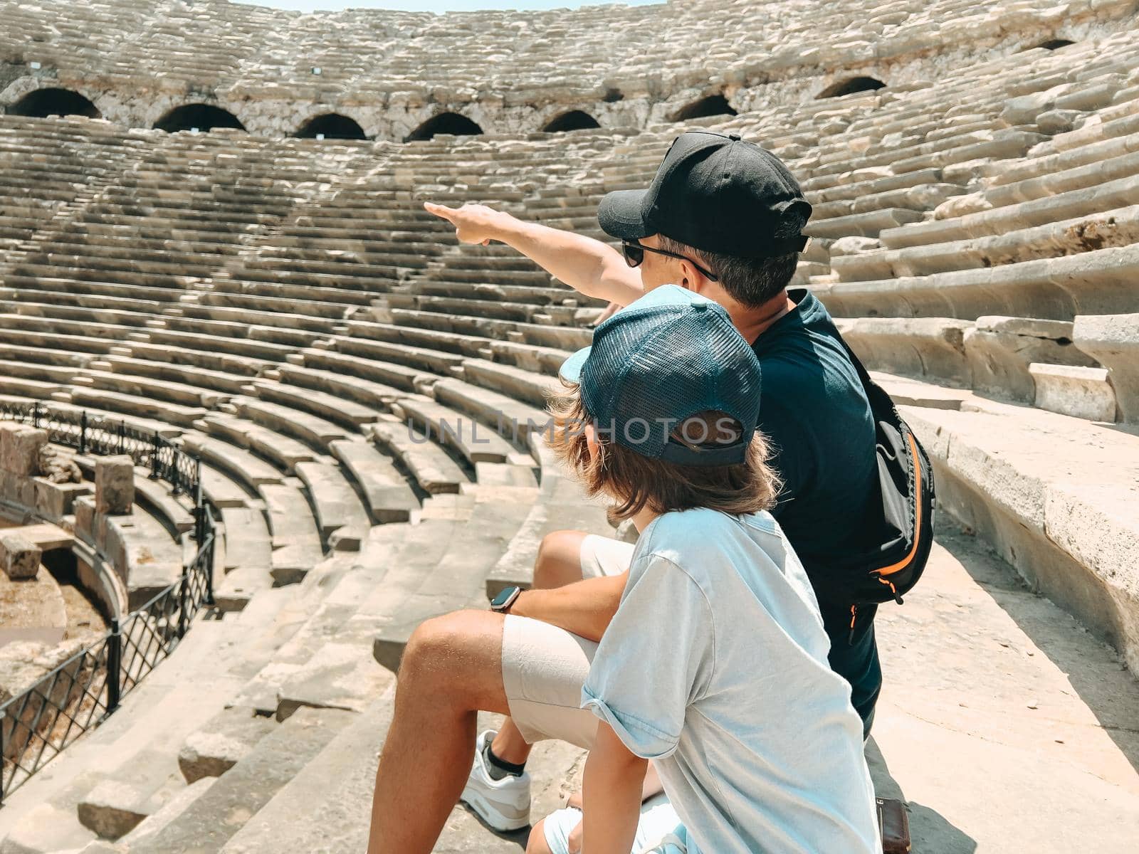 Young father dad and his school boy kid son tourists visiting ancient antique coliseum amphitheater ruins in hot summer day.