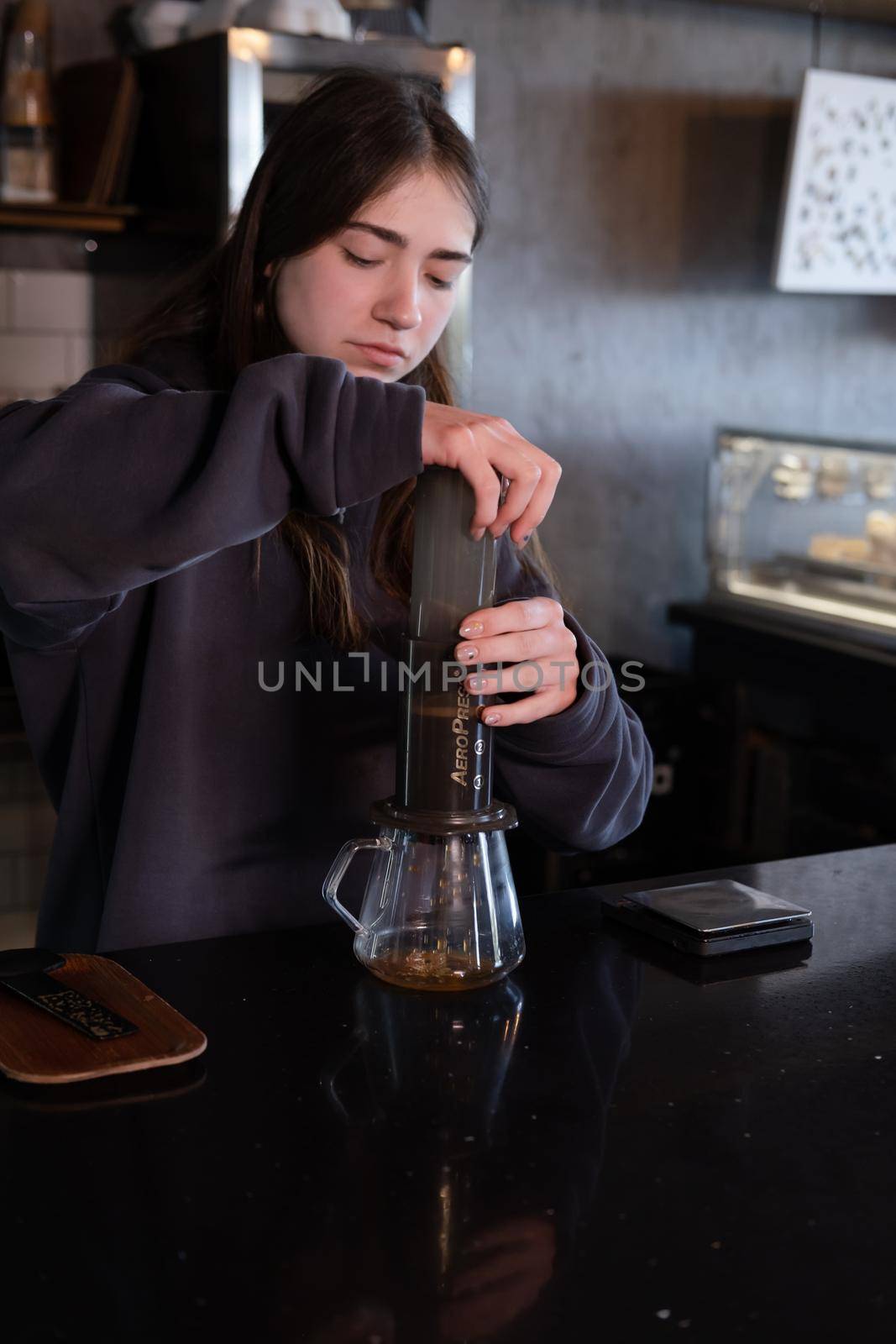 pretty brunette girl making aeropress coffee in modern coffee shop.