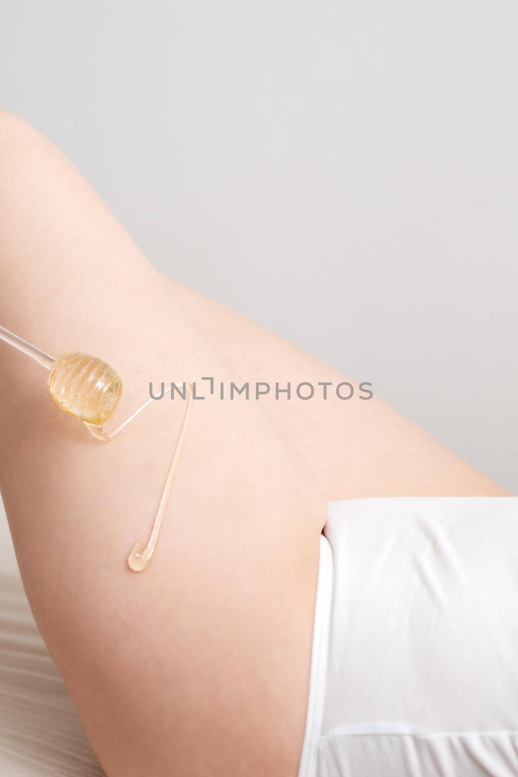 Wax on honey stick flowing down on female leg in human hand wearing protective glove on white background