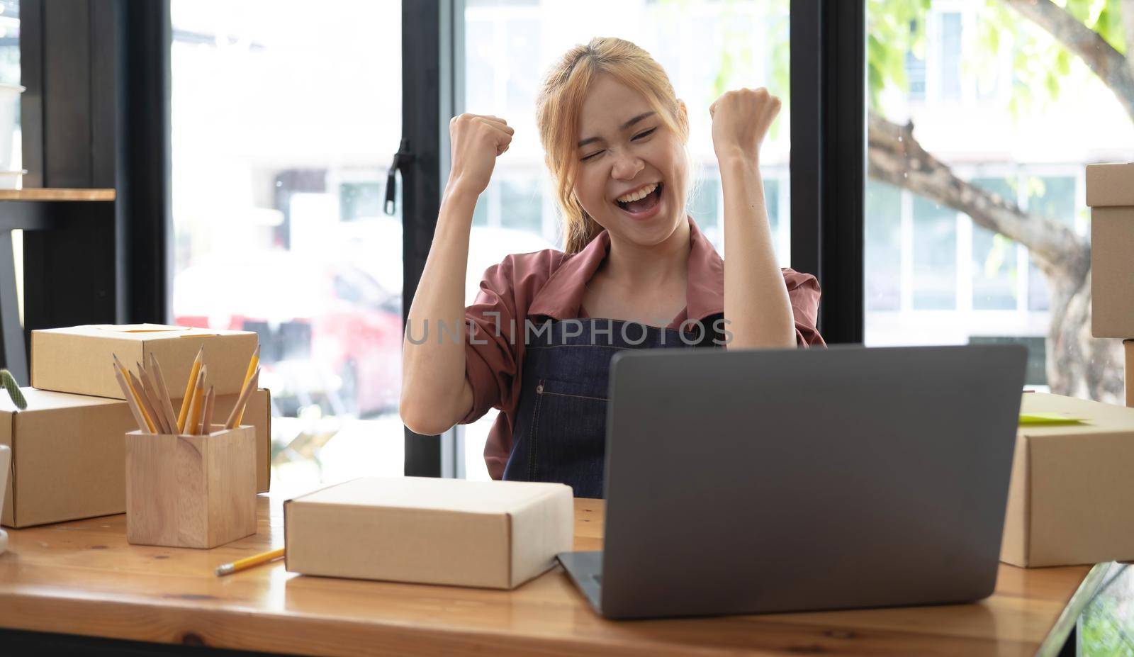 Happy young asian woman startup small business freelance holding parcel box and computer laptop and sitting on chair, Online marketing packing box delivery concept.