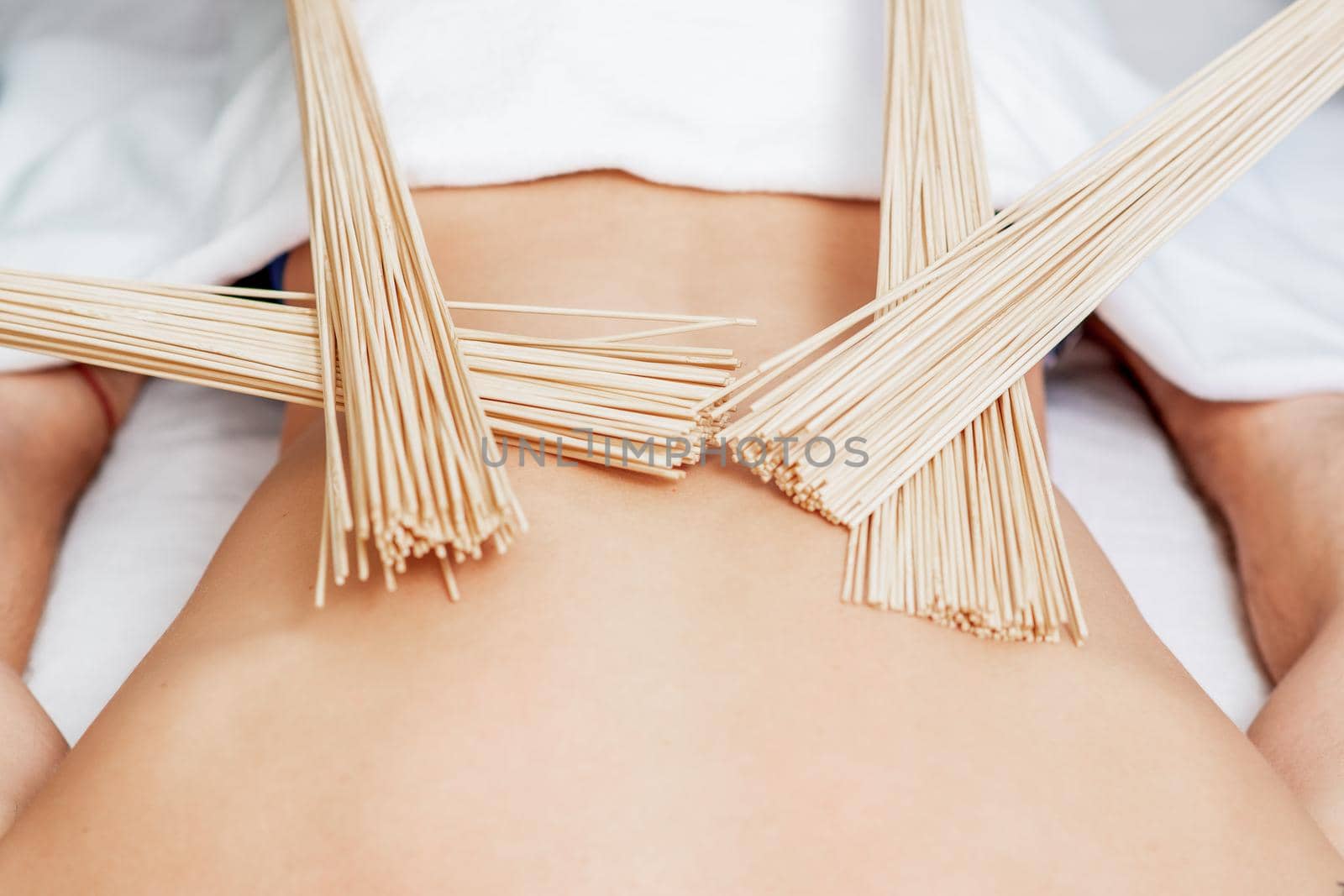 Bamboo brooms on back of young man during massage in four hands