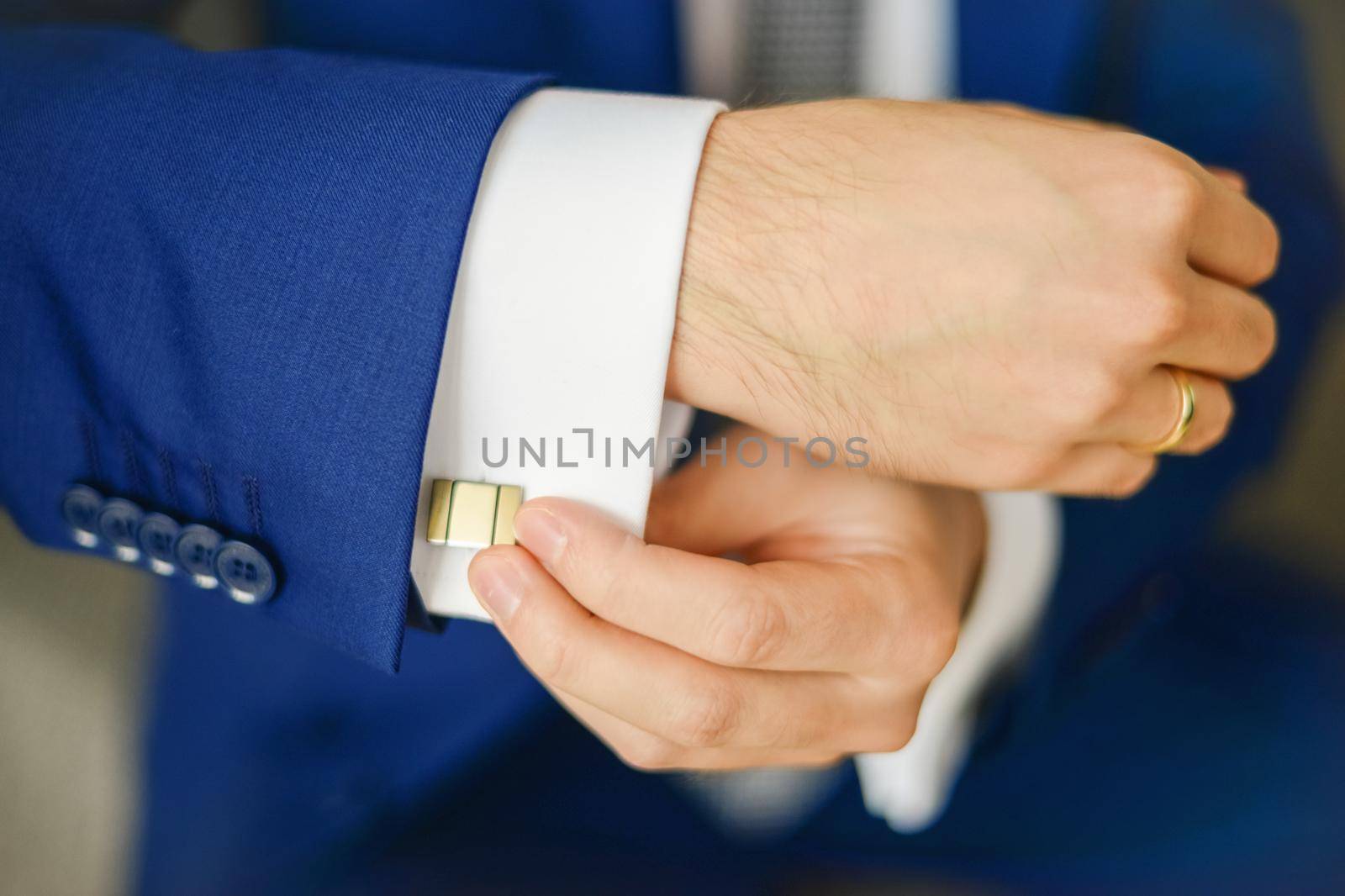Groom or businessman fasten cufflink on the cuff of the shirt wearing blue suit