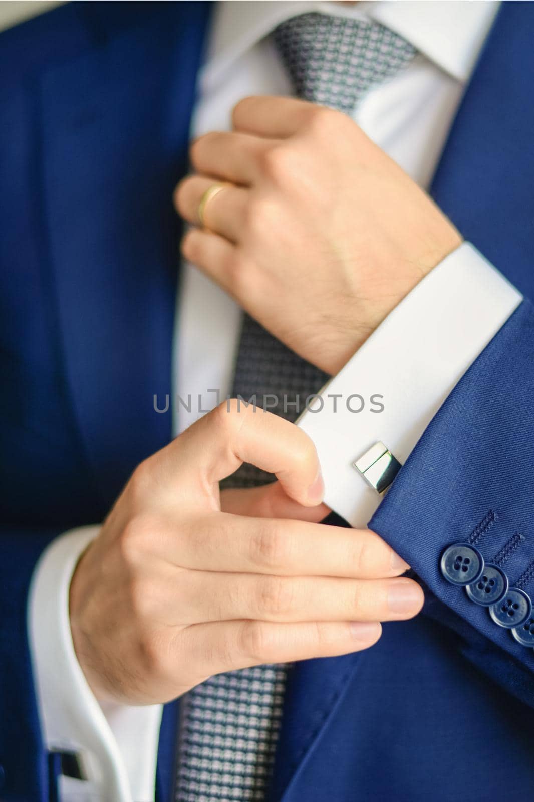 Groom or businessman fasten cufflink on the cuff of the shirt wearing blue suit