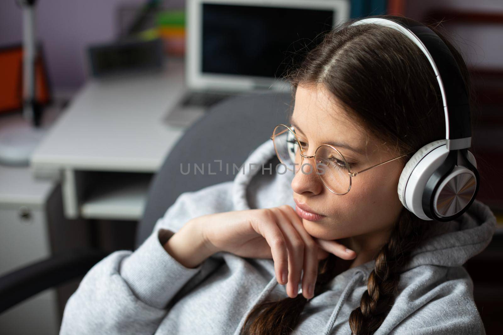 A teenage girl listens to music on headphones with complete seriousness. Young girl in pigtails and glasses concerned during music message.