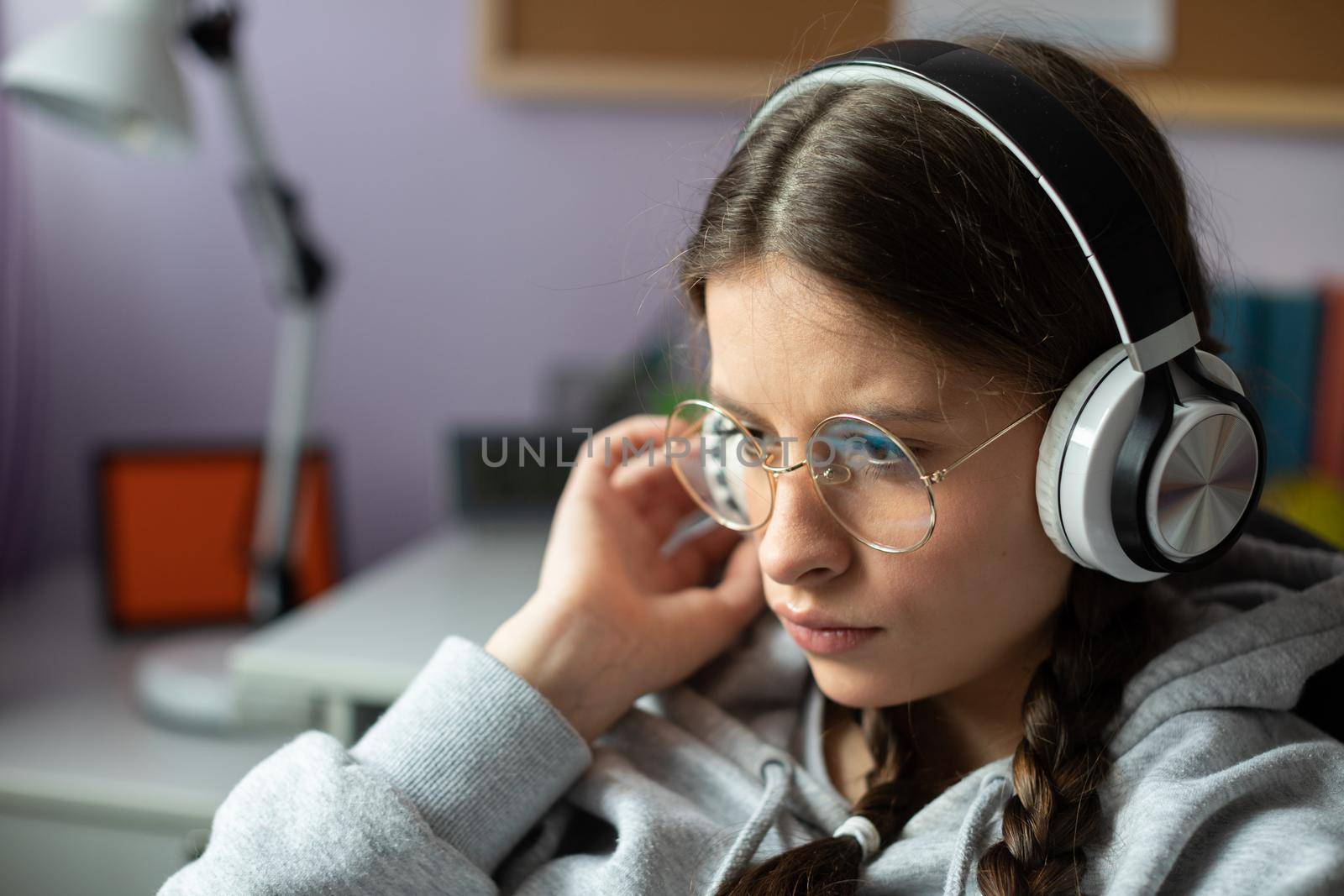 A brunette girl listens intently to a new song by her favorite music band. A young girl with braids and glasses listens to music.