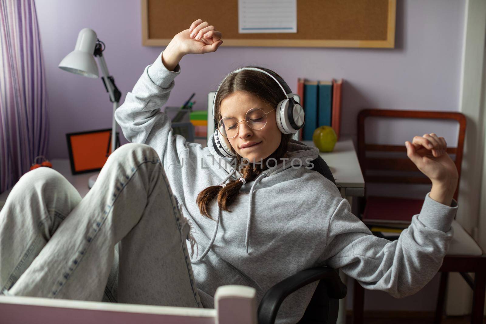 A teen raises her hands while listening to music. Musical emotion is translated into verbal emotion. A young girl with braids and glasses listens to music.