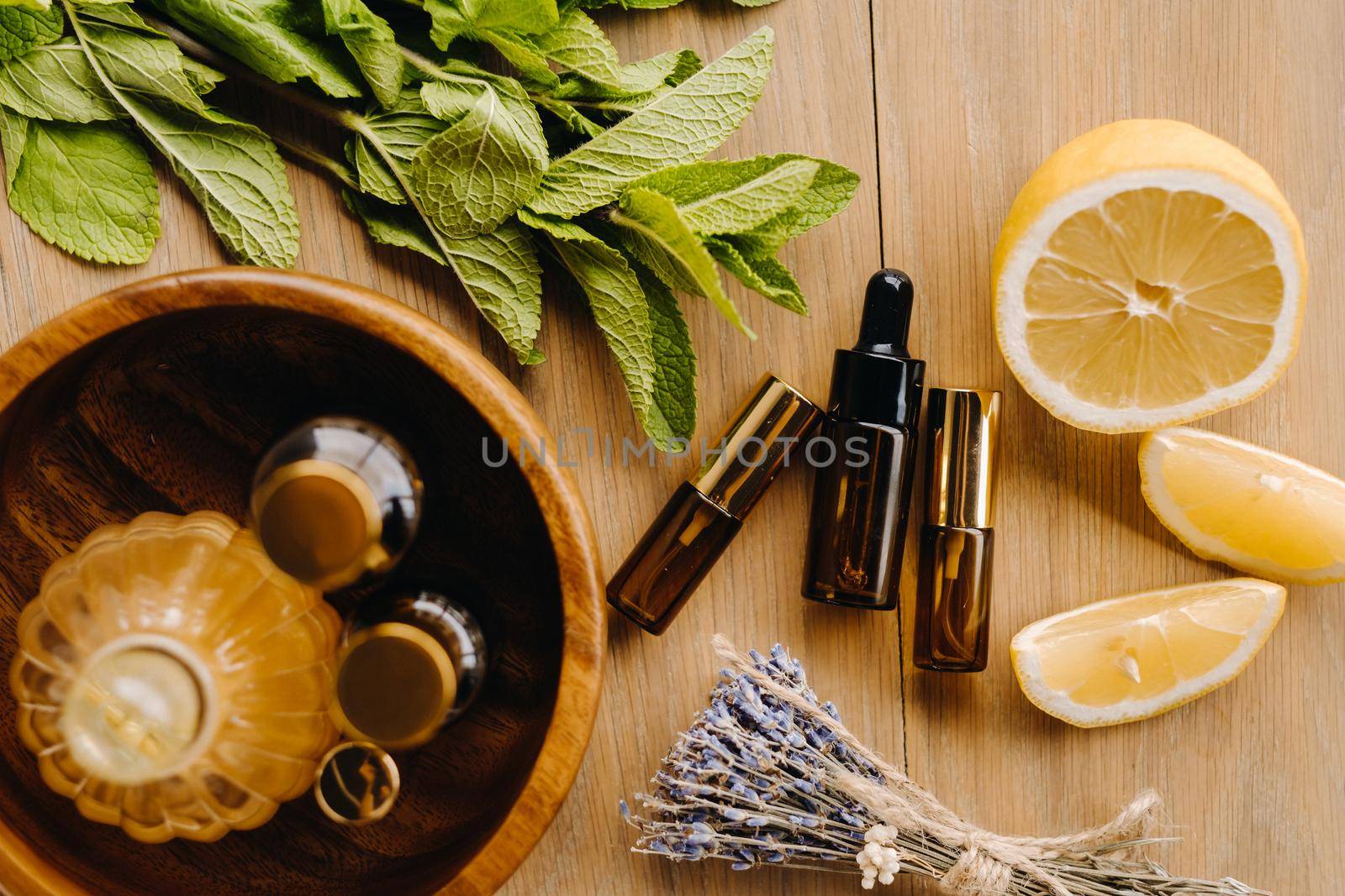 Essential oil in bottles with the aroma of lemon, mint and lavender, lying on a wooden surface.