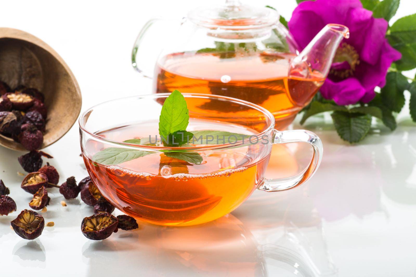 brewed rosehip tea in a glass teapot with rosehip flowers and mint, isolated on white background.