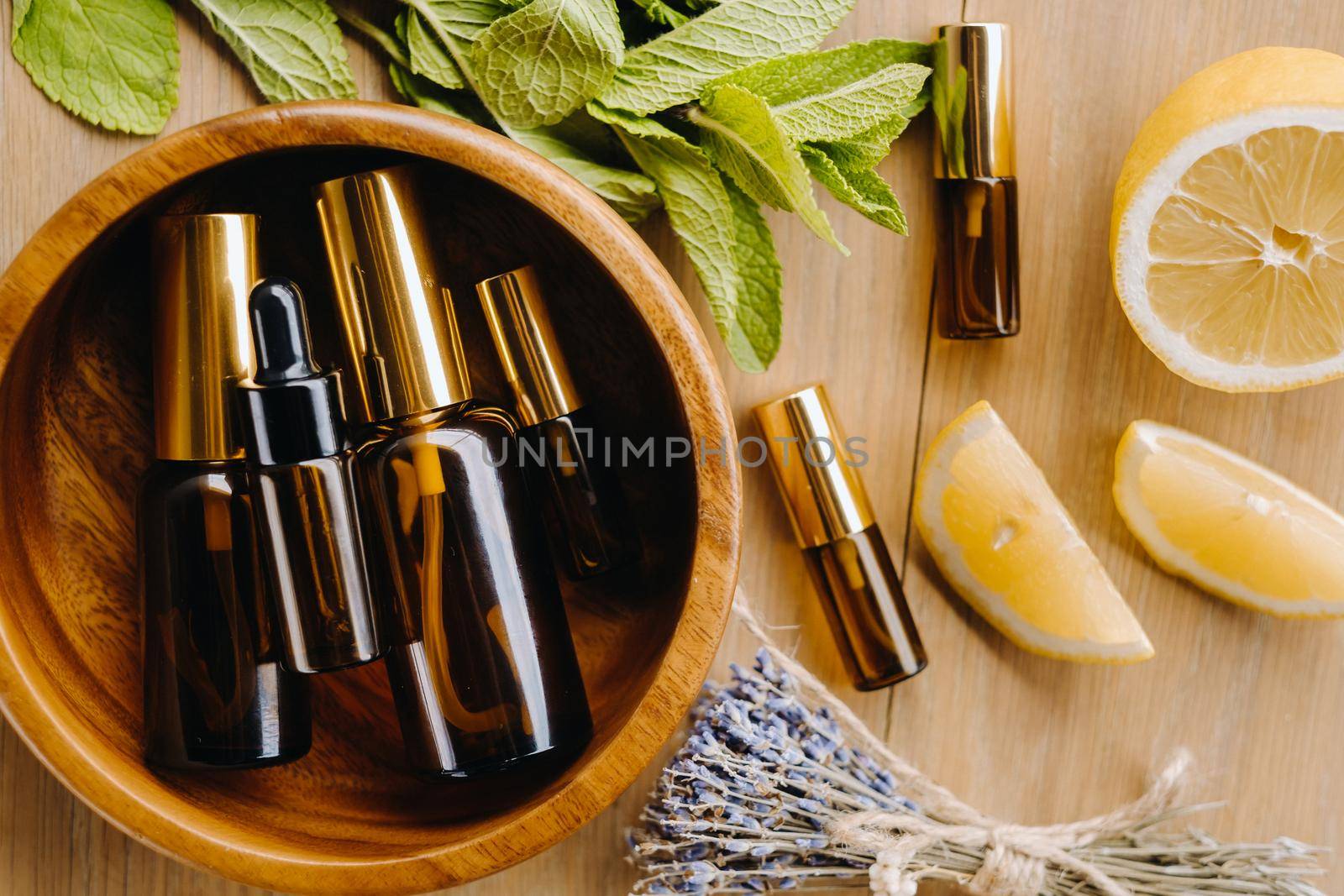 Essential oil in bottles with the aroma of lemon, mint and lavender, lying on a wooden surface.
