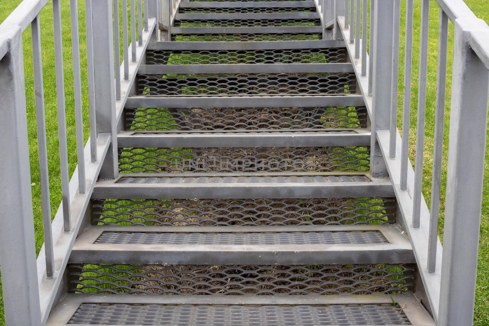 Grey iron staircase with railings on a green grass background.