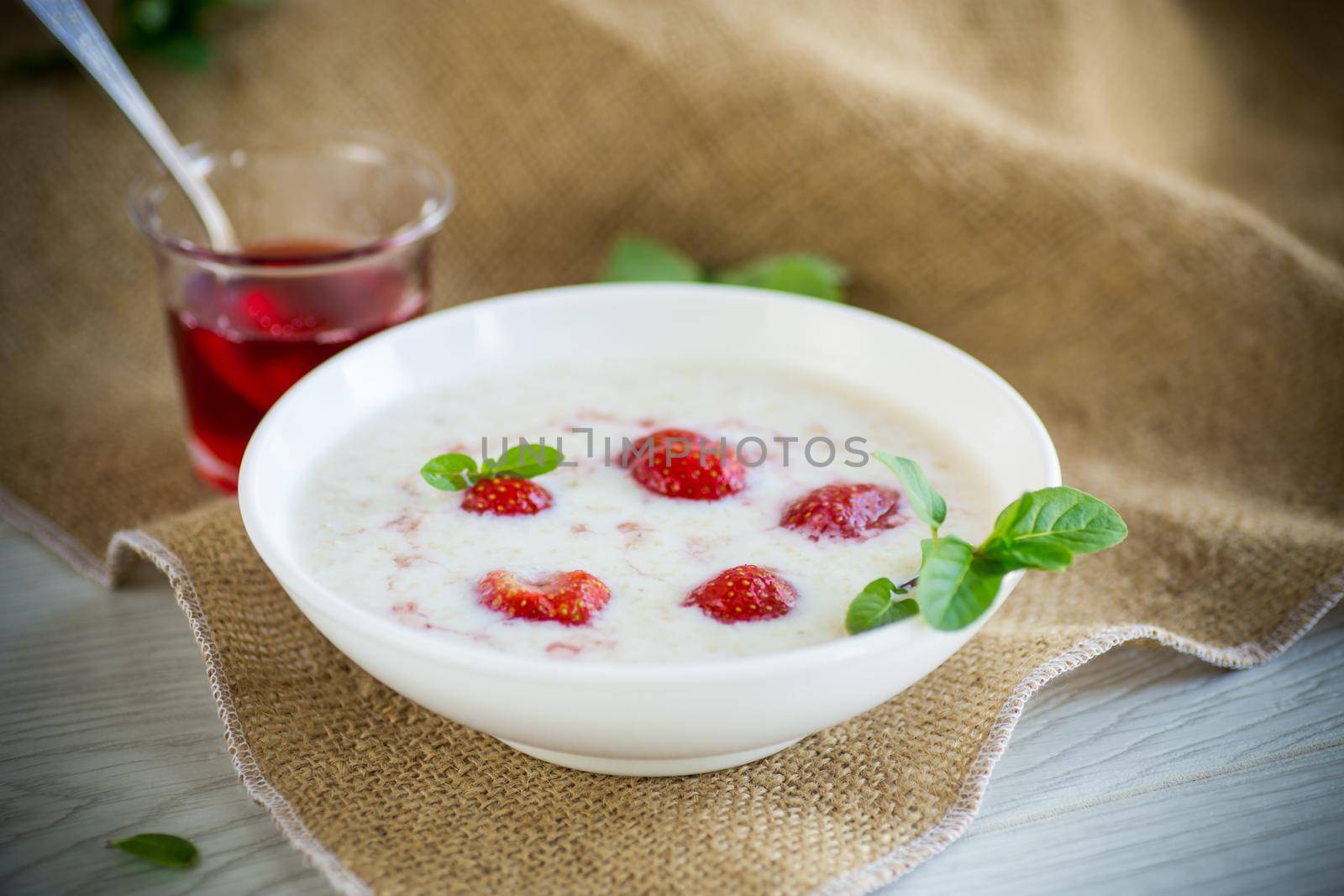 sweet milk oatmeal with strawberries in a plate, on a wooden table.