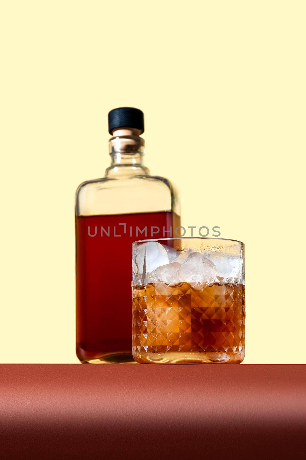 Bottle and Glass with Whiskey and Ice on Brown Table on Light Background. Modern Style. Creative Concept.