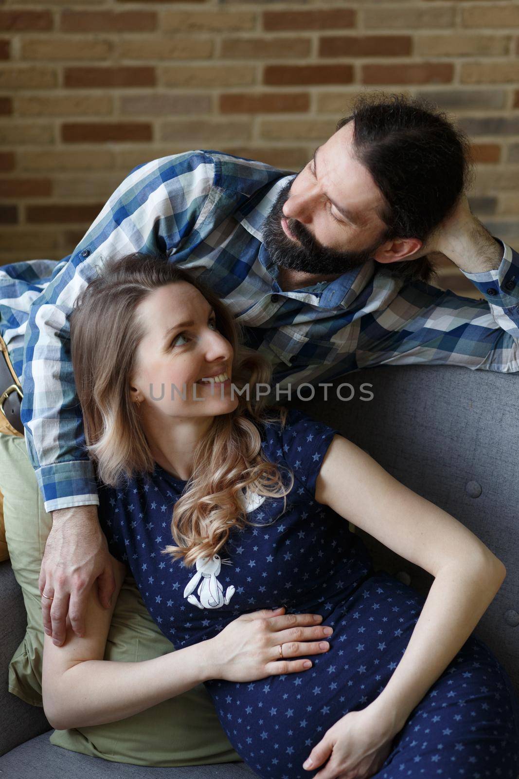 An adult couple in love waiting for a child. A man and his pregnant wife are playing on a sofa at home