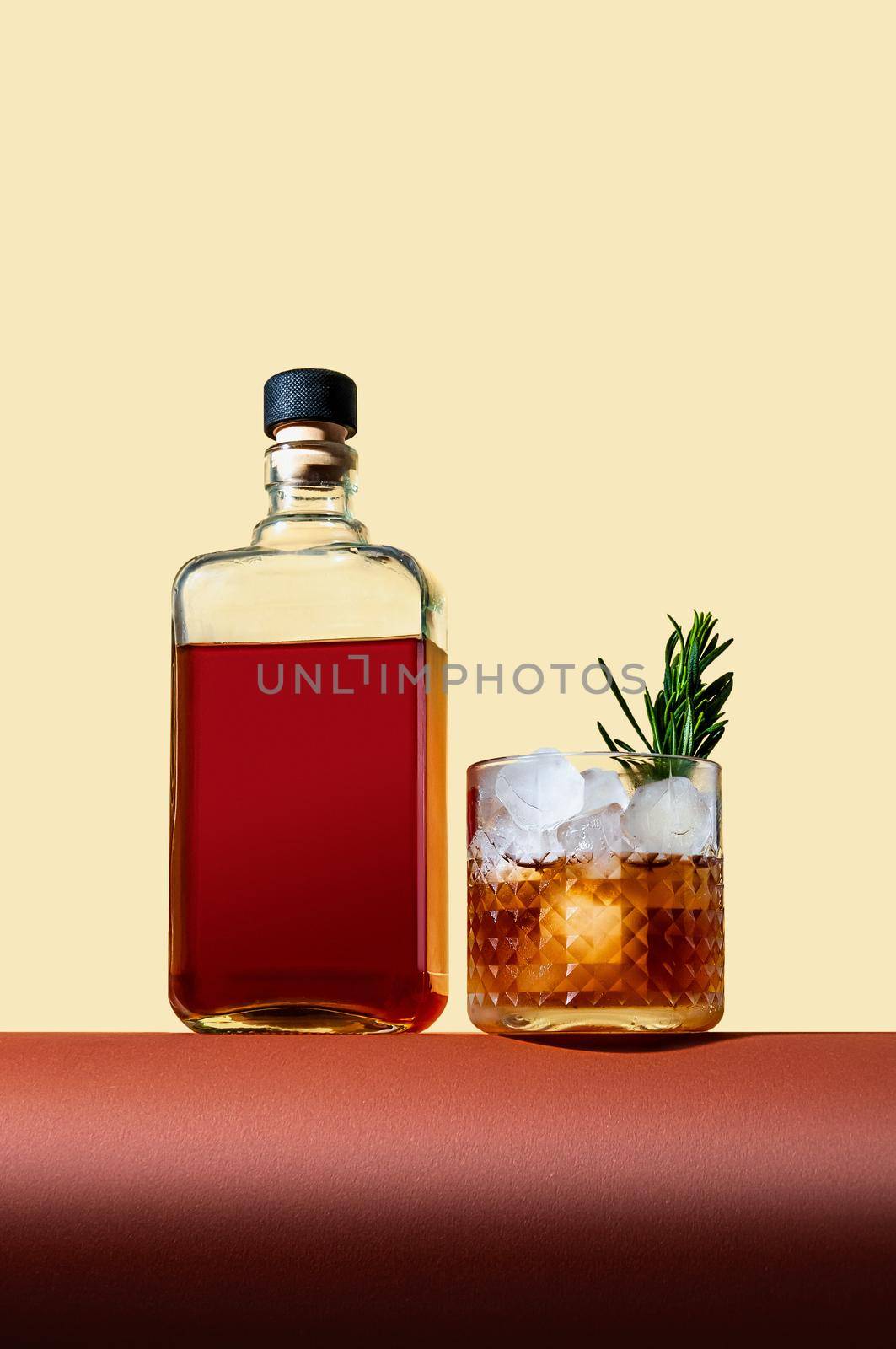 Bottle and Glass with Whiskey and Ice on Brown Table on Light Background. Modern Style. Creative Concept.