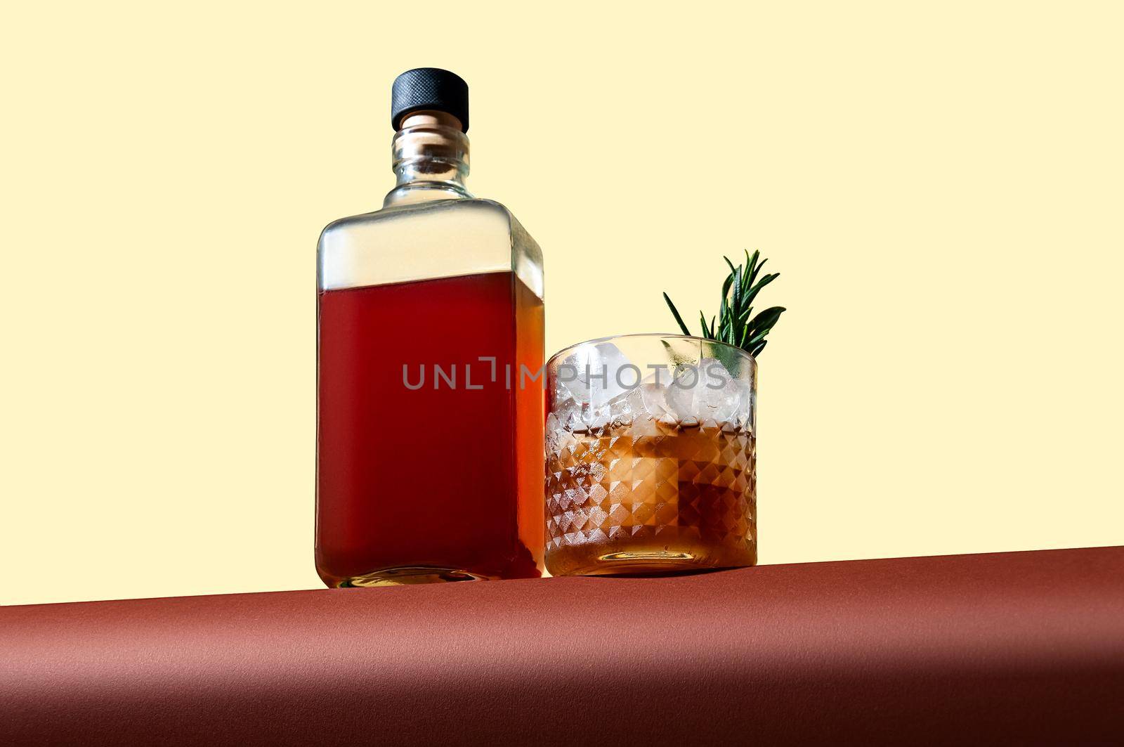 Bottle and Glass with Whiskey and Ice on Brown Table on Light Background. Modern Style. Creative Concept.