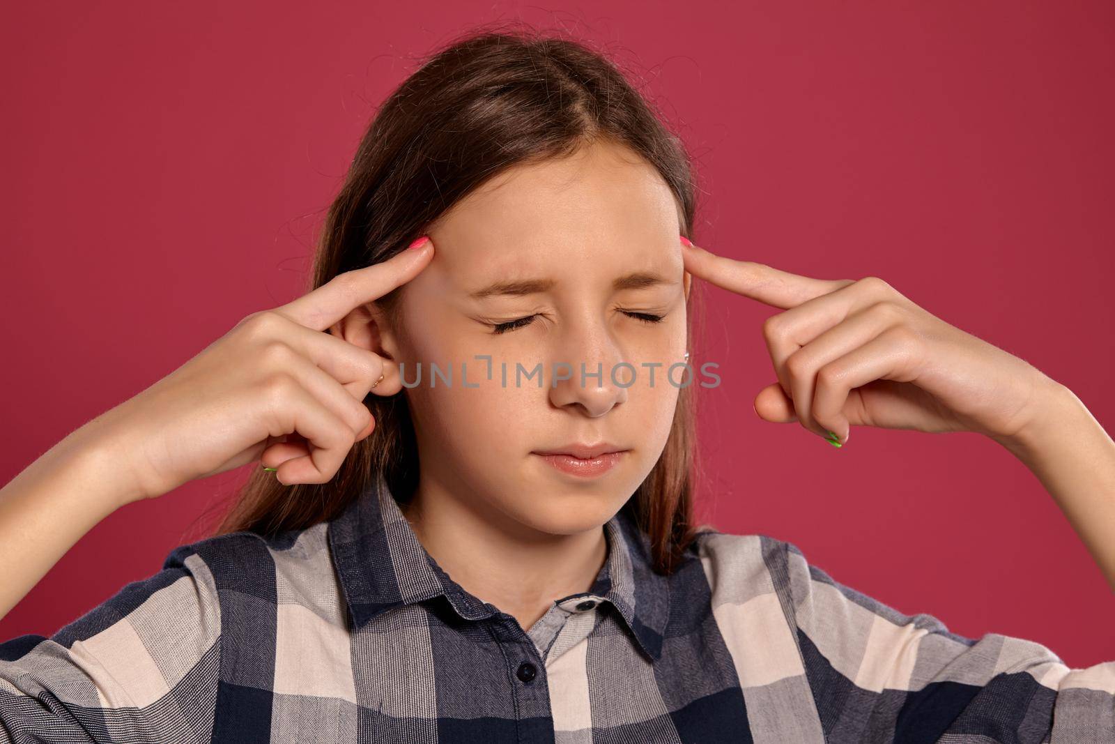 Close-up portrait of a charming teenager in a casual checkered shirt posing with closed eyes against a pink studio background. Long hair, healthy clean skin and brown eyes. Sincere emotions concept. Copy space.