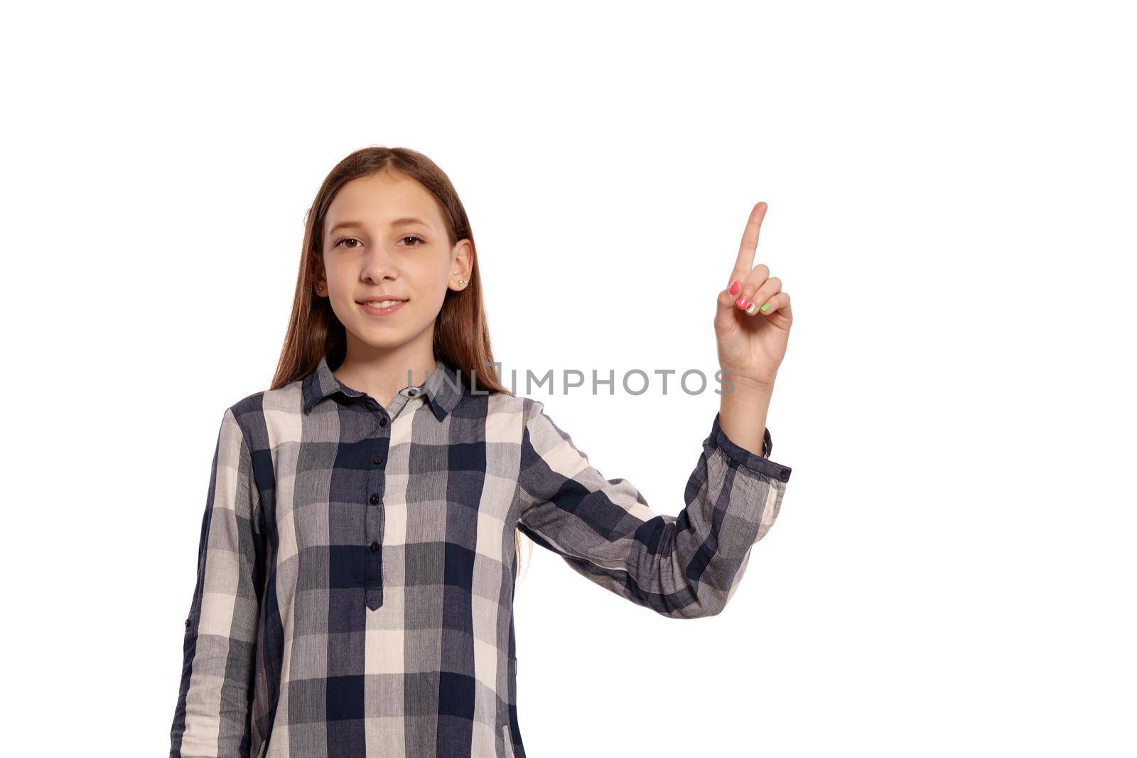 Portrait of a cute teenage lady in a casual checkered shirt posing with raised index finger isolated on white studio background. Long hair, healthy clean skin and brown eyes. Sincere emotions concept. Copy space.