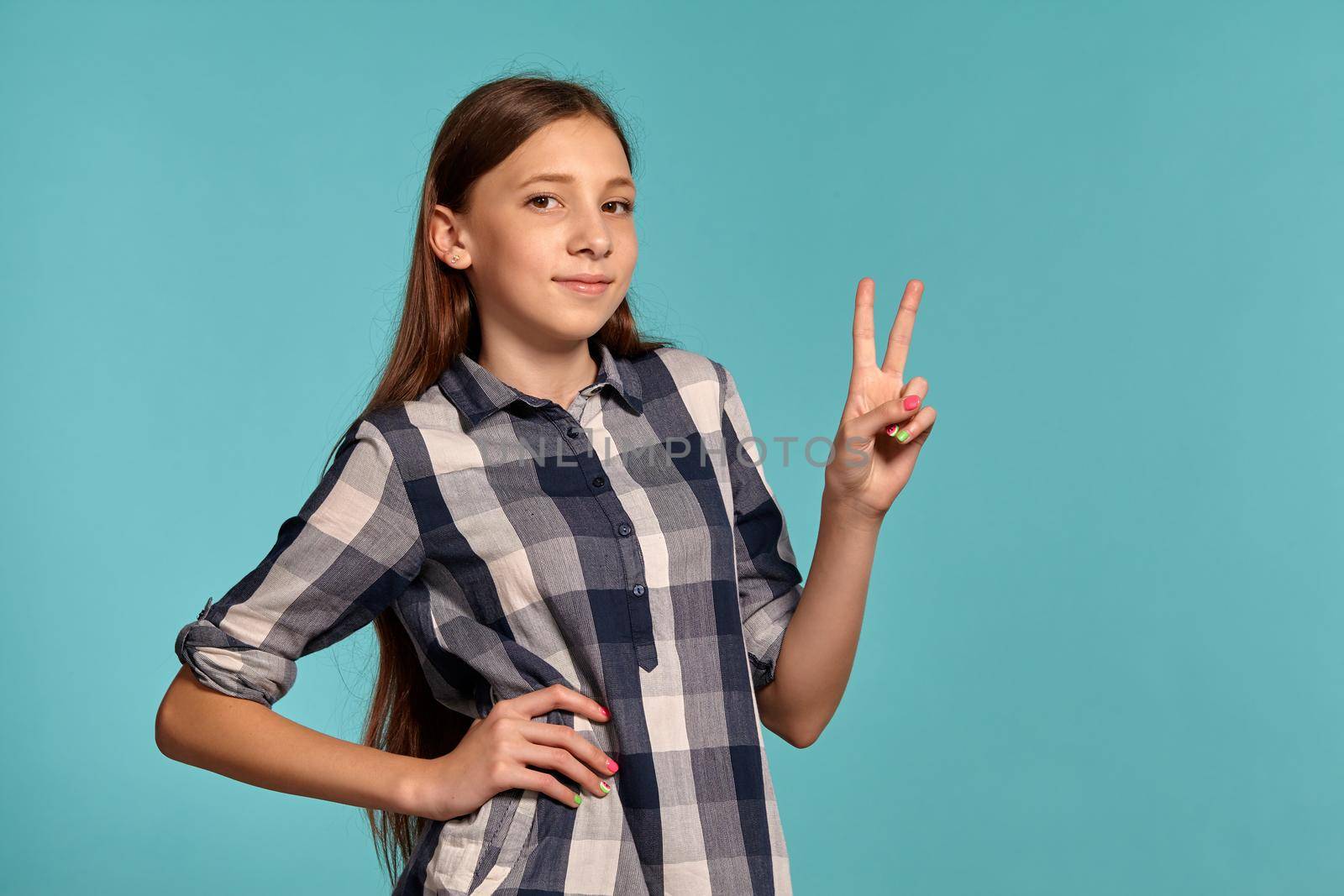 Beautiful teenage girl in a casual checkered shirt is posing against a blue studio background. by nazarovsergey