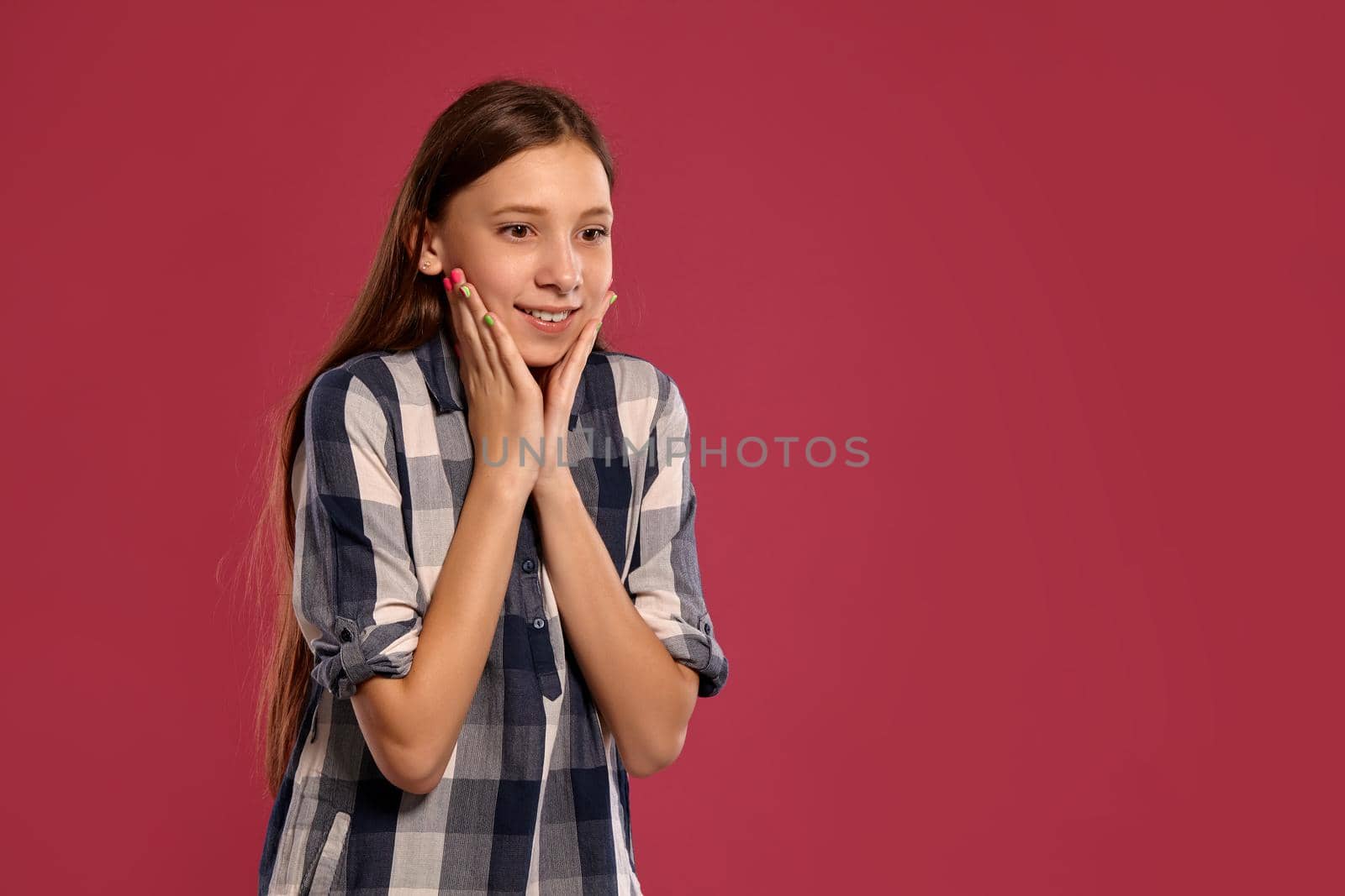 Portrait of an attractive teenage female in a casual checkered shirt looking wondered while posing against a pink studio background. Long hair, healthy clean skin and brown eyes. Sincere emotions concept. Copy space.