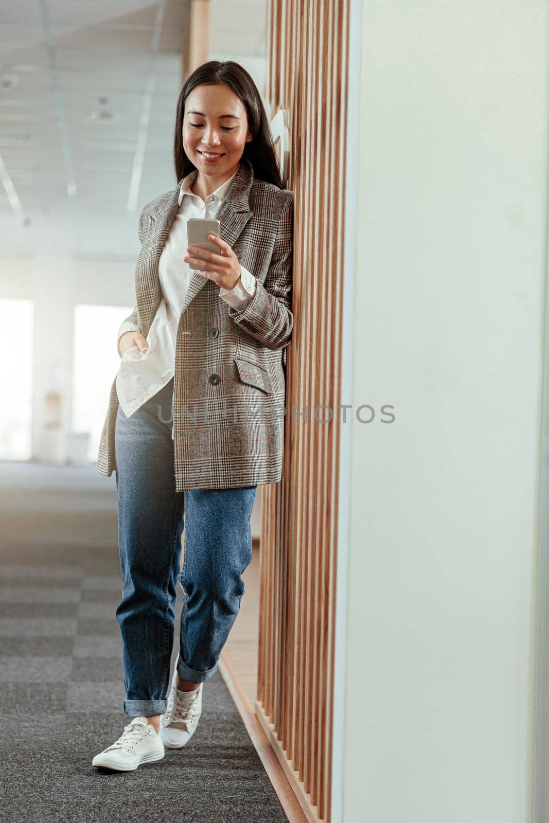 Portrait of smiling asian business woman standing in modern office with phone. High quality photo