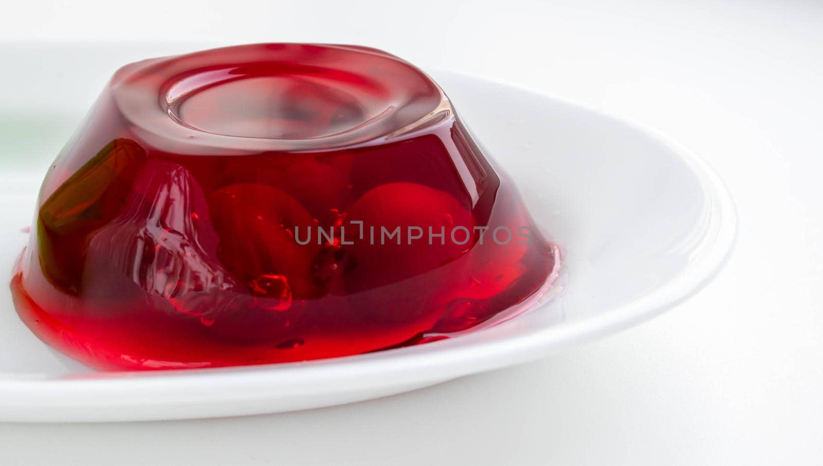 White plate with cherry berries in red jelly on a white background