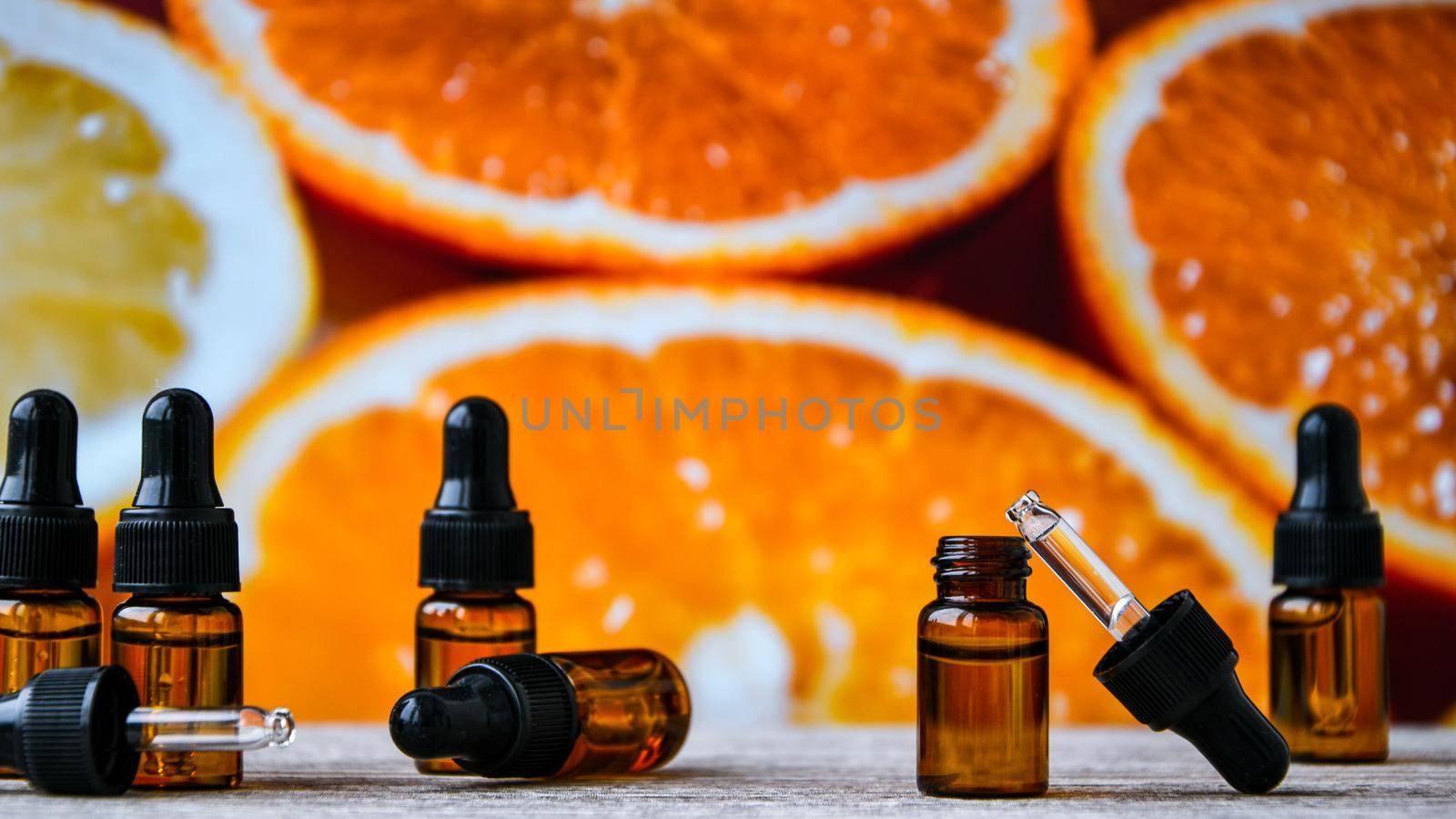 Bottle of essential oil from oranges on wooden background with pieces of oranges - alternative medicine. Essential aroma oil with oranges. Citrus oil for skin care, spa, wellness, massage, aromatherapy and natural medicine
