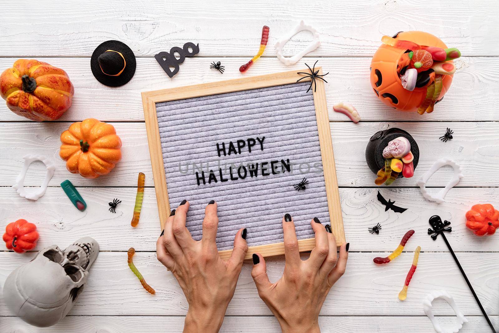 Halloween concept. Happy Halloween words on gray letter board with scary woman hands candy flat lay on wooden background