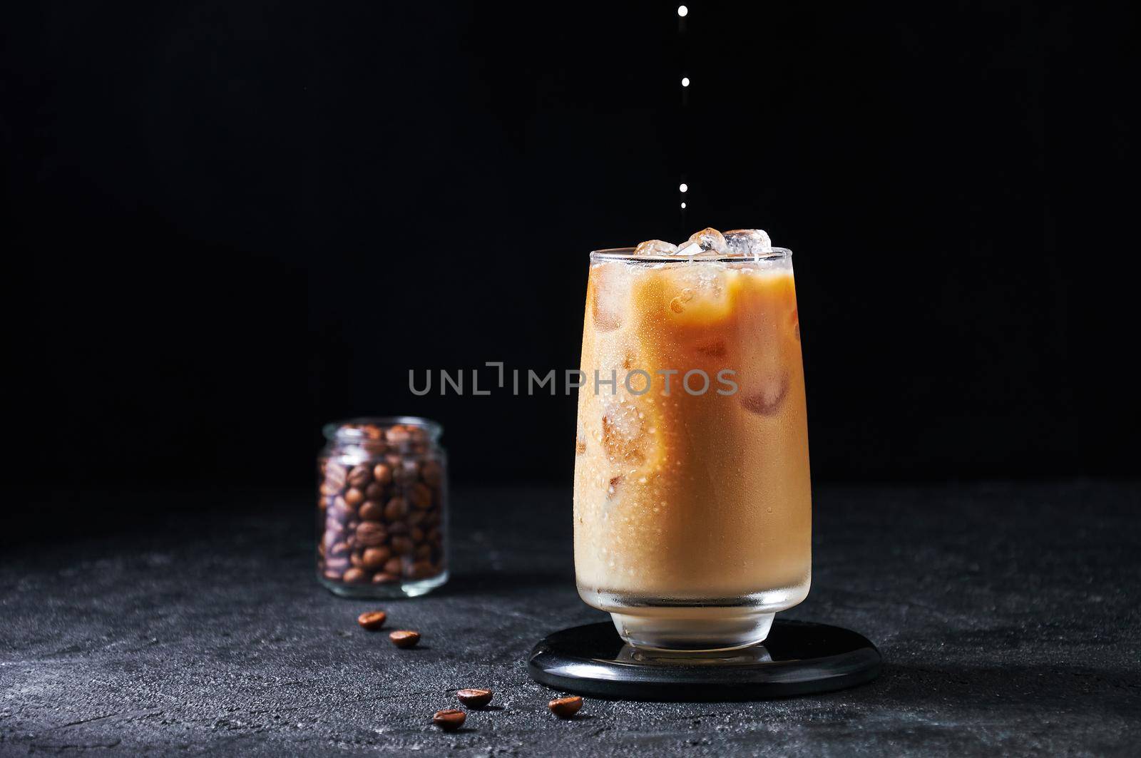 Cold Summer Drink. Iced Coffee with Milk Drops in Tall Glass on Dark Background. Drinks in Motion. Copy Spase.