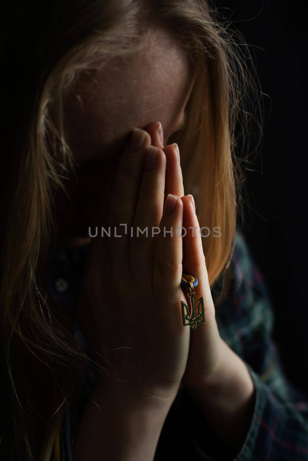 Ukrainian blonde woman prays for Ukraine during the war with the state emblem Trident in her hands. Russia attacked Ukraine on February 24, 2022