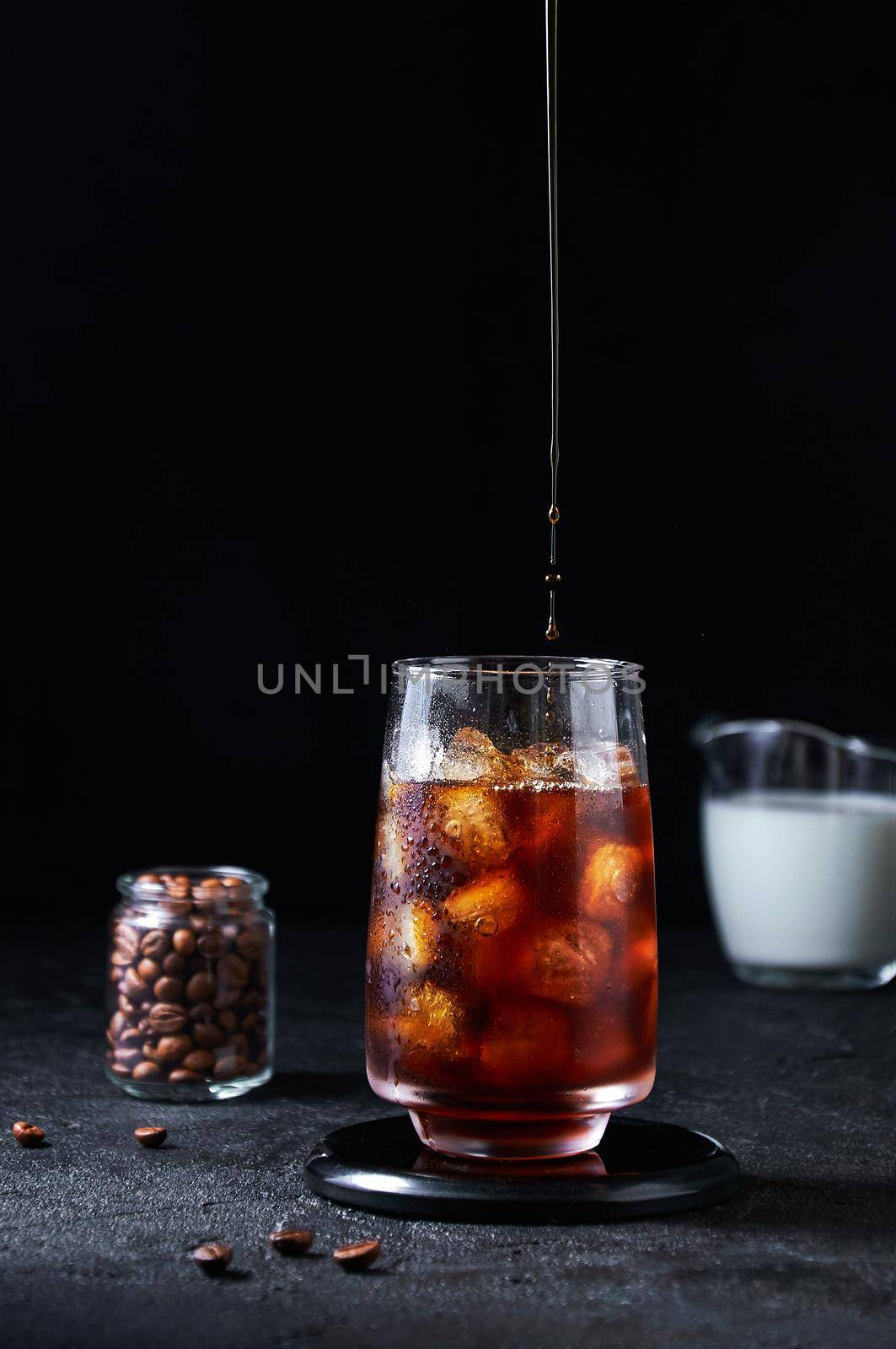 Iced Coffee Pouring into Tall Glass on Dark Background. Concept Refreshing Summer Drink.