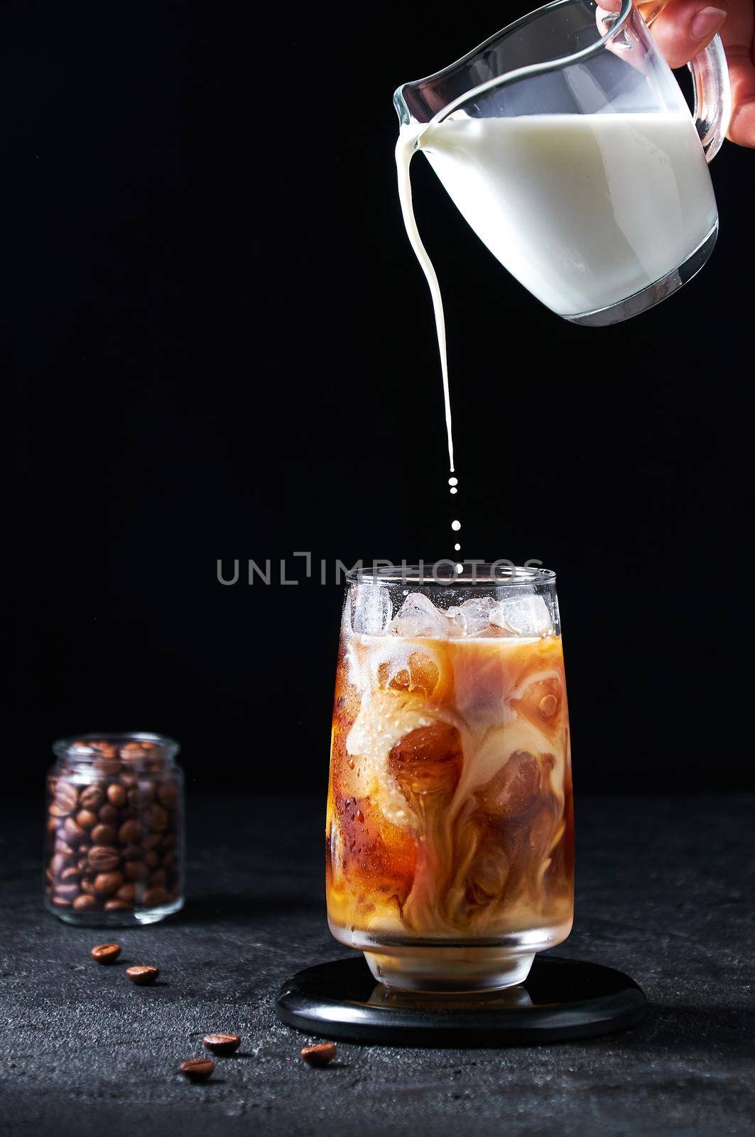 Cold Summer Drink. Iced Coffee with Pouring Milk in Tall Glass on Dark Background. Drinks in Motion.