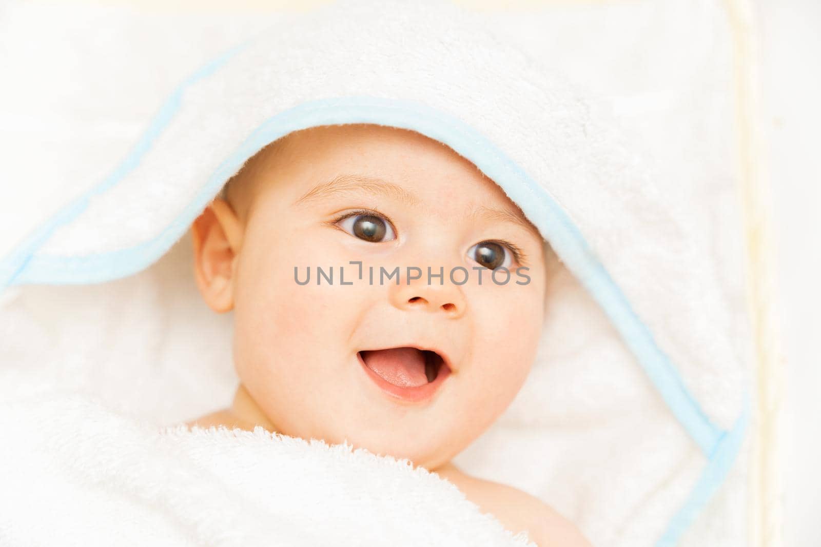 Baby boy wearing diaper and blue towel in white sunny bedroom. Newborn child relaxing in bed after bath or shower. Nursery for children. New born kid with toy bear. High quality photo