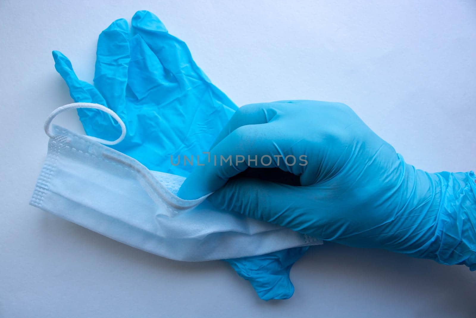A man's hand in a blue latex glove holds a mask on a white background. Protect your hands and face from viruses.
